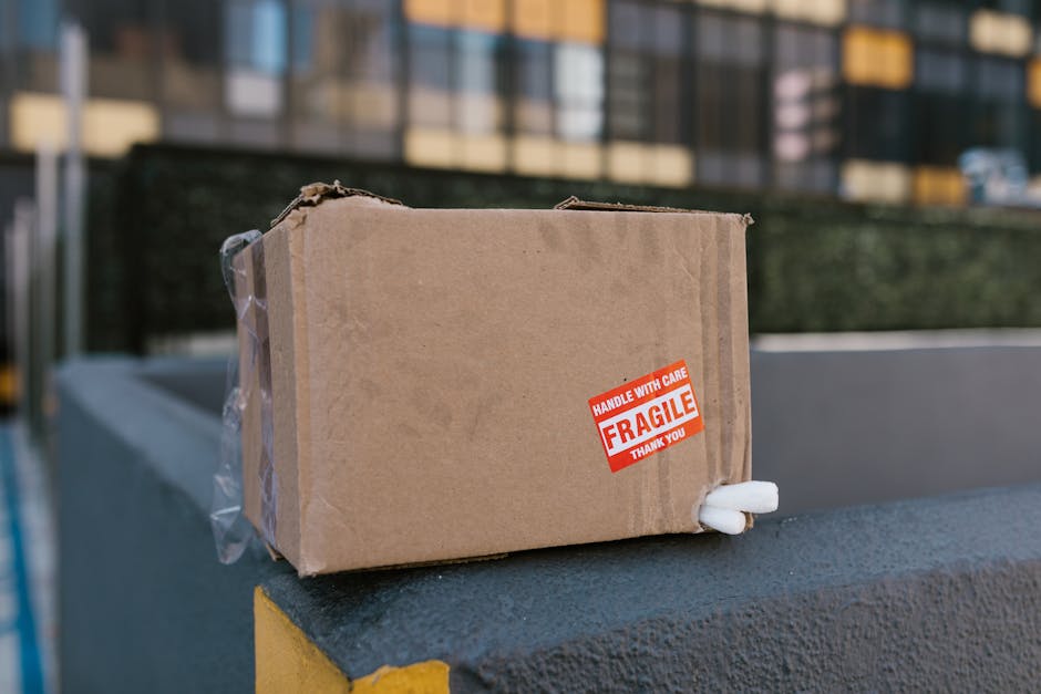 Close-up of a person's hands carefully wrapping a flat, rectangular object, possibly a fragile electronic device or picture frame, in brown packing paper during a home relocation or packing process. T